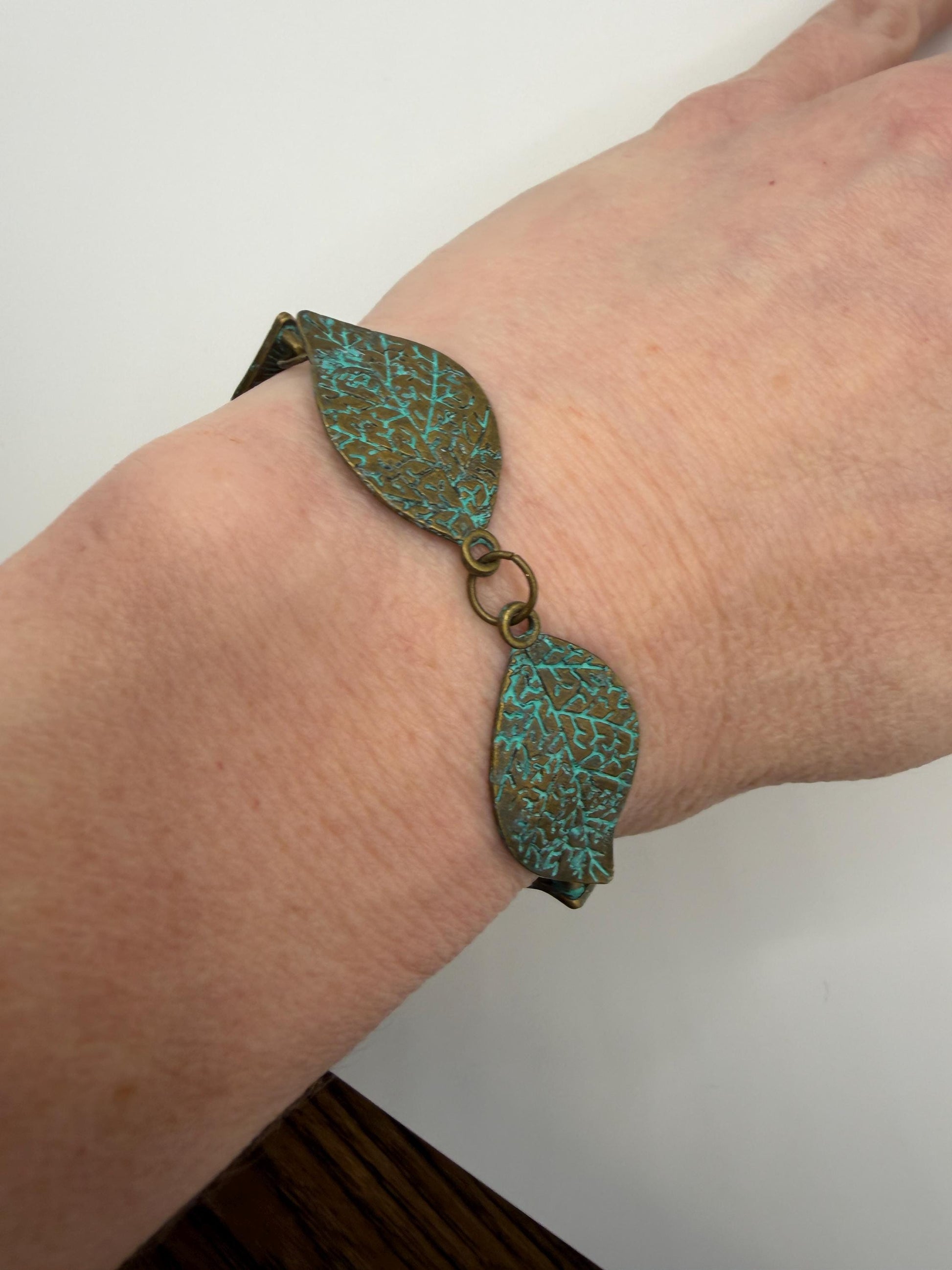 Bracelet with leaf-shaped turquoise stones on a wrist against a neutral background