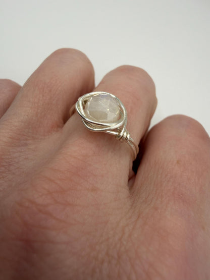 Silver ring with a large gemstone on a finger against a white background