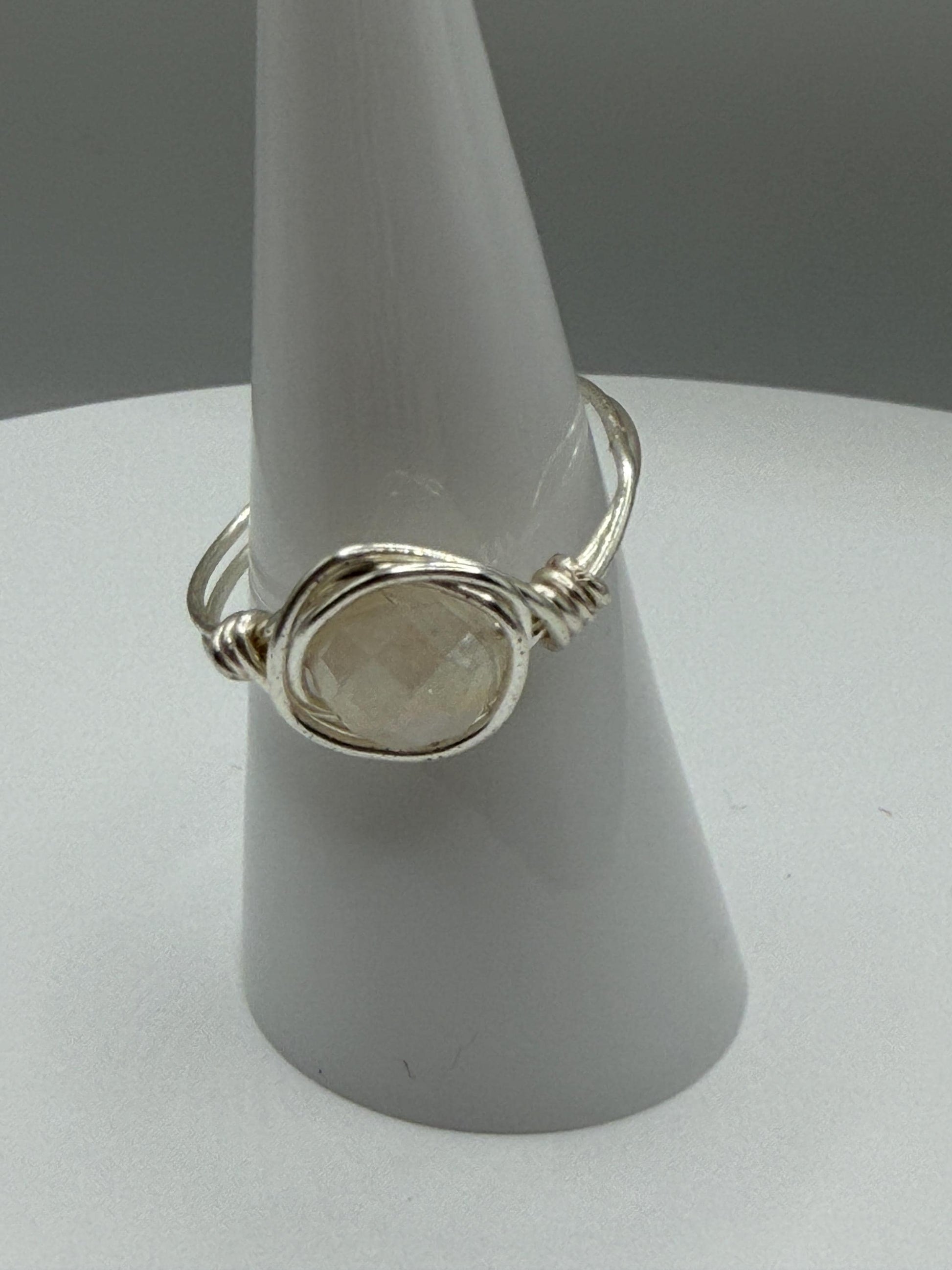 Silver ring with a stone on a gray stand against a gray background
