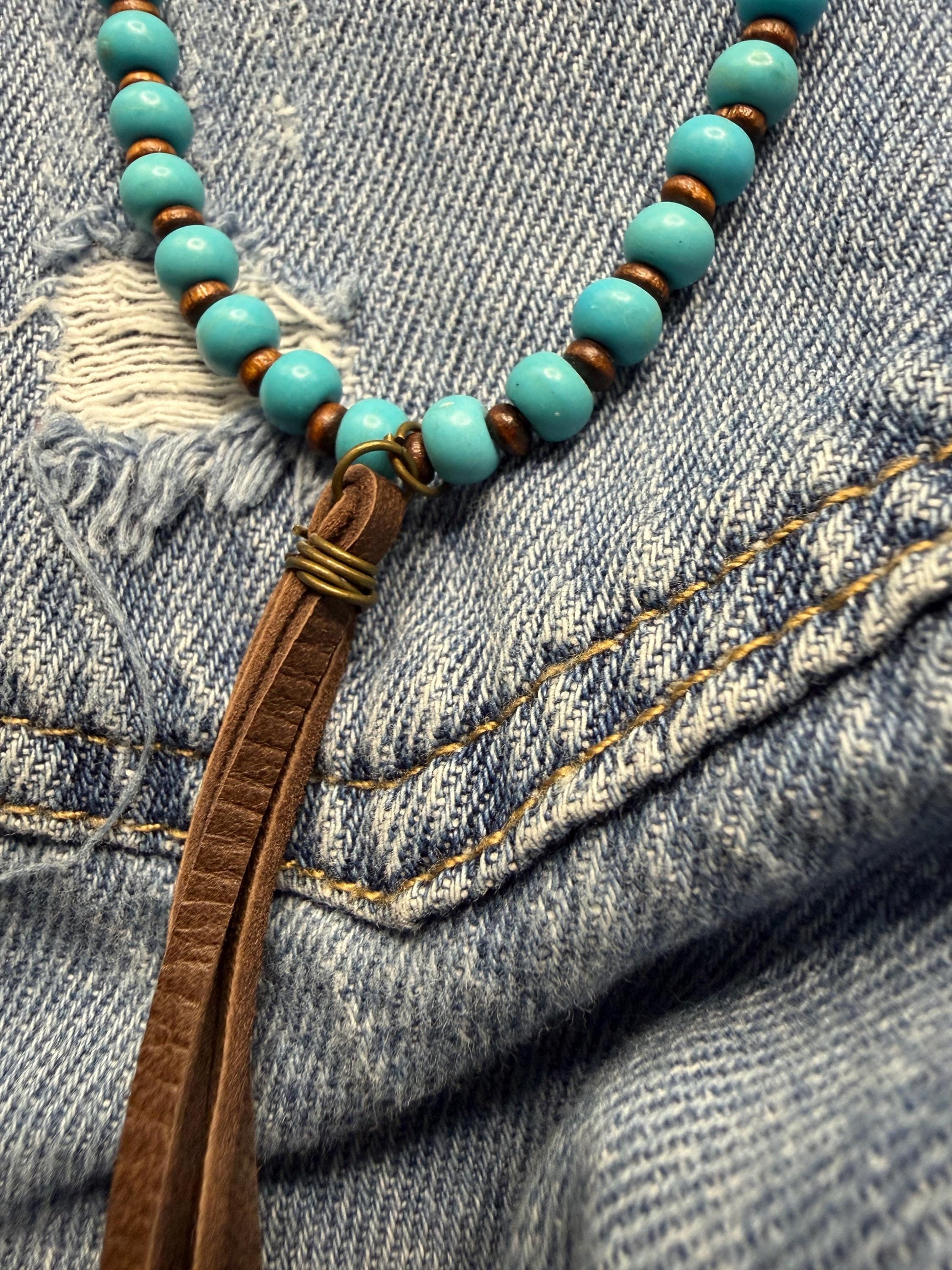 Turquoise beaded necklace with brown leather cord on denim fabric
