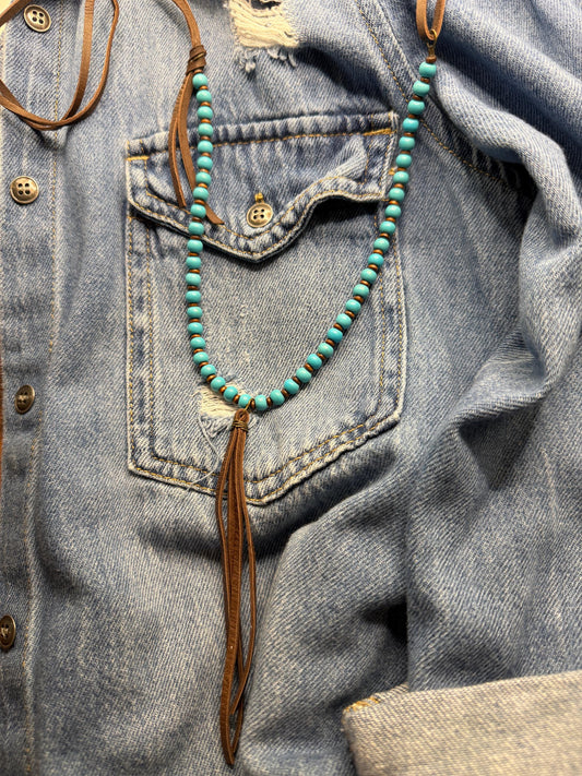 Turquoise beaded necklace with a feather pendant on a denim jacket.