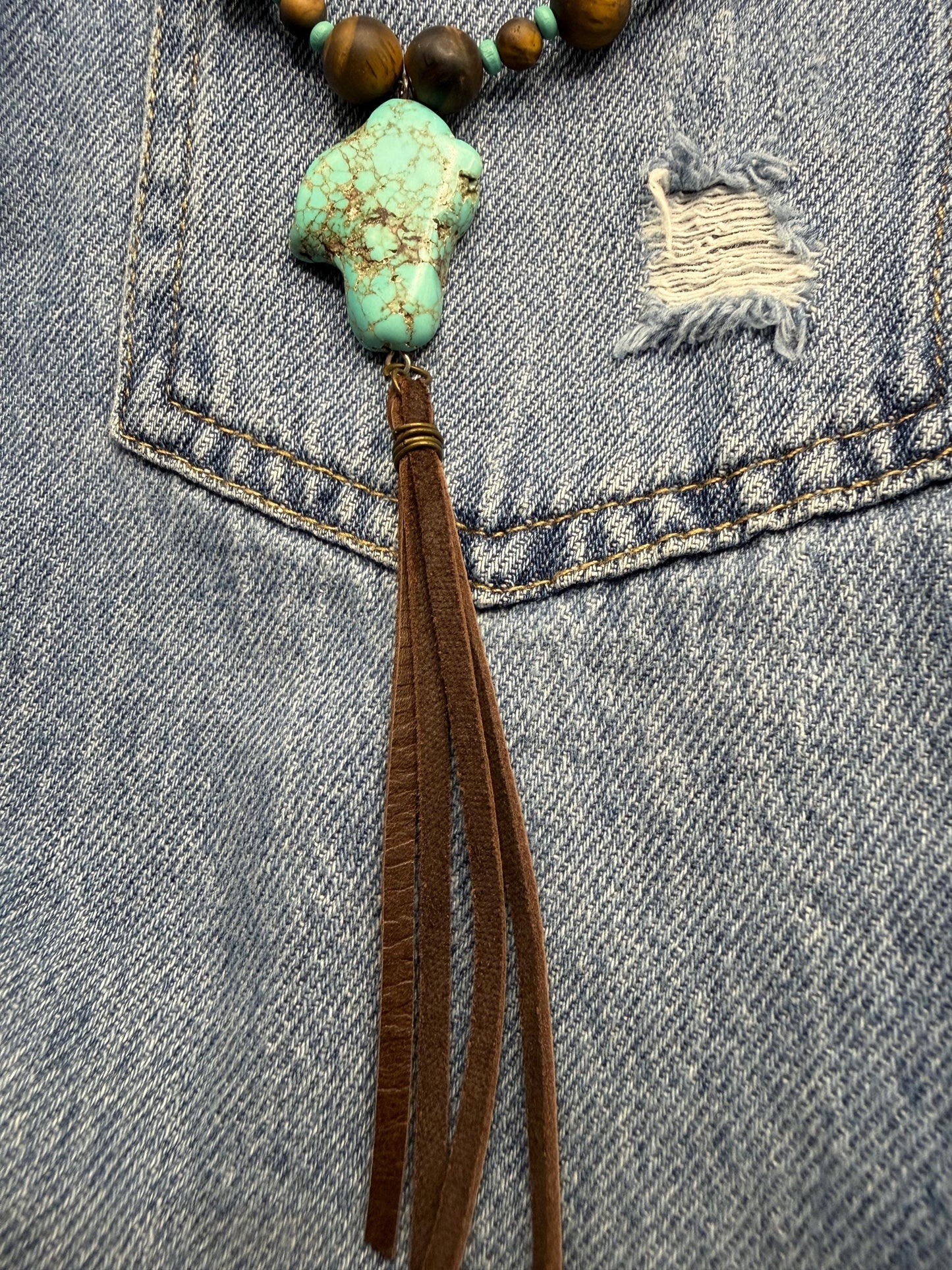 Necklace with turquoise pendant and brown tassel on denim fabric
