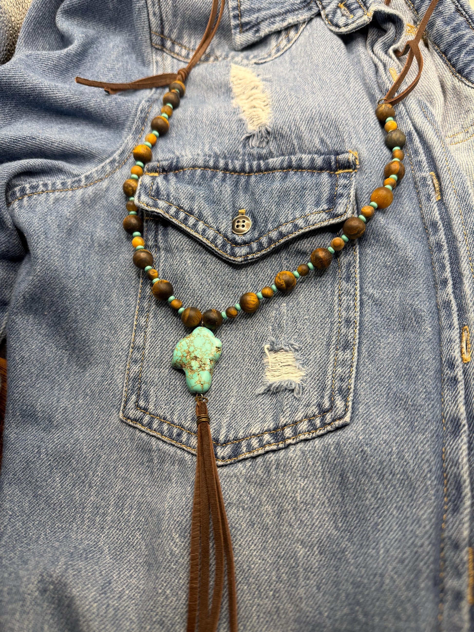 Necklace with beads and tassel hanging from a denim jacket pocket