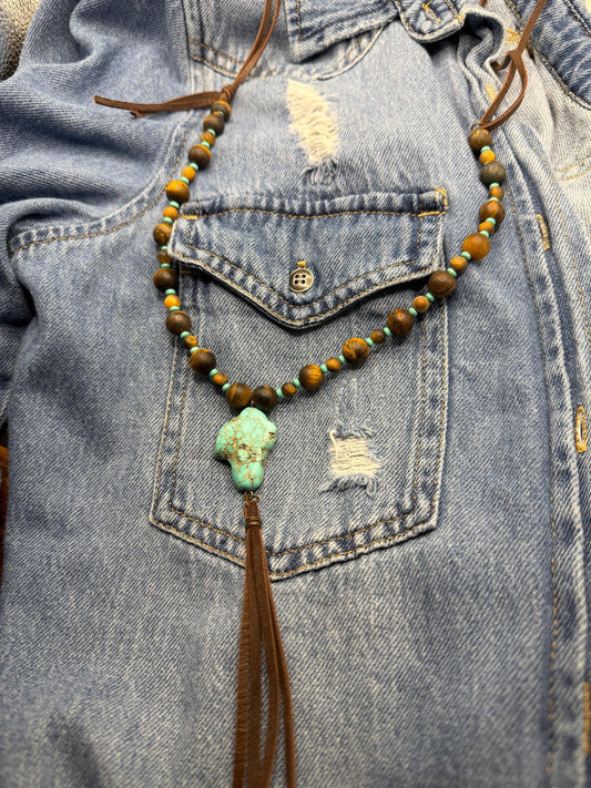 Necklace with beads and tassel hanging from a denim jacket pocket