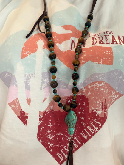 Beaded necklace with a turquoise pendant on a shirt with motivational text.