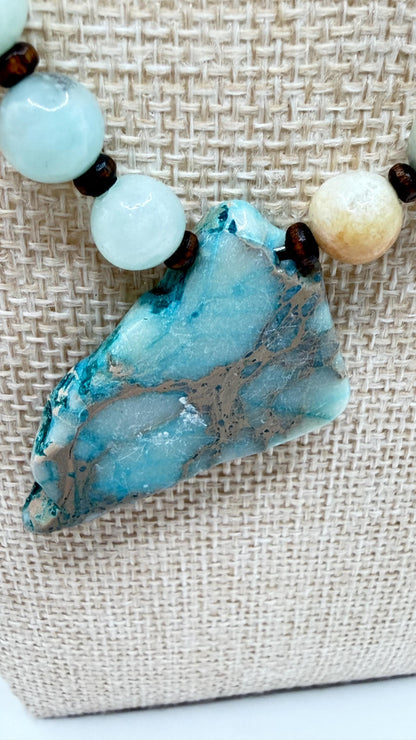 Necklace with a large blue stone pendant and smaller beads on a textured fabric background