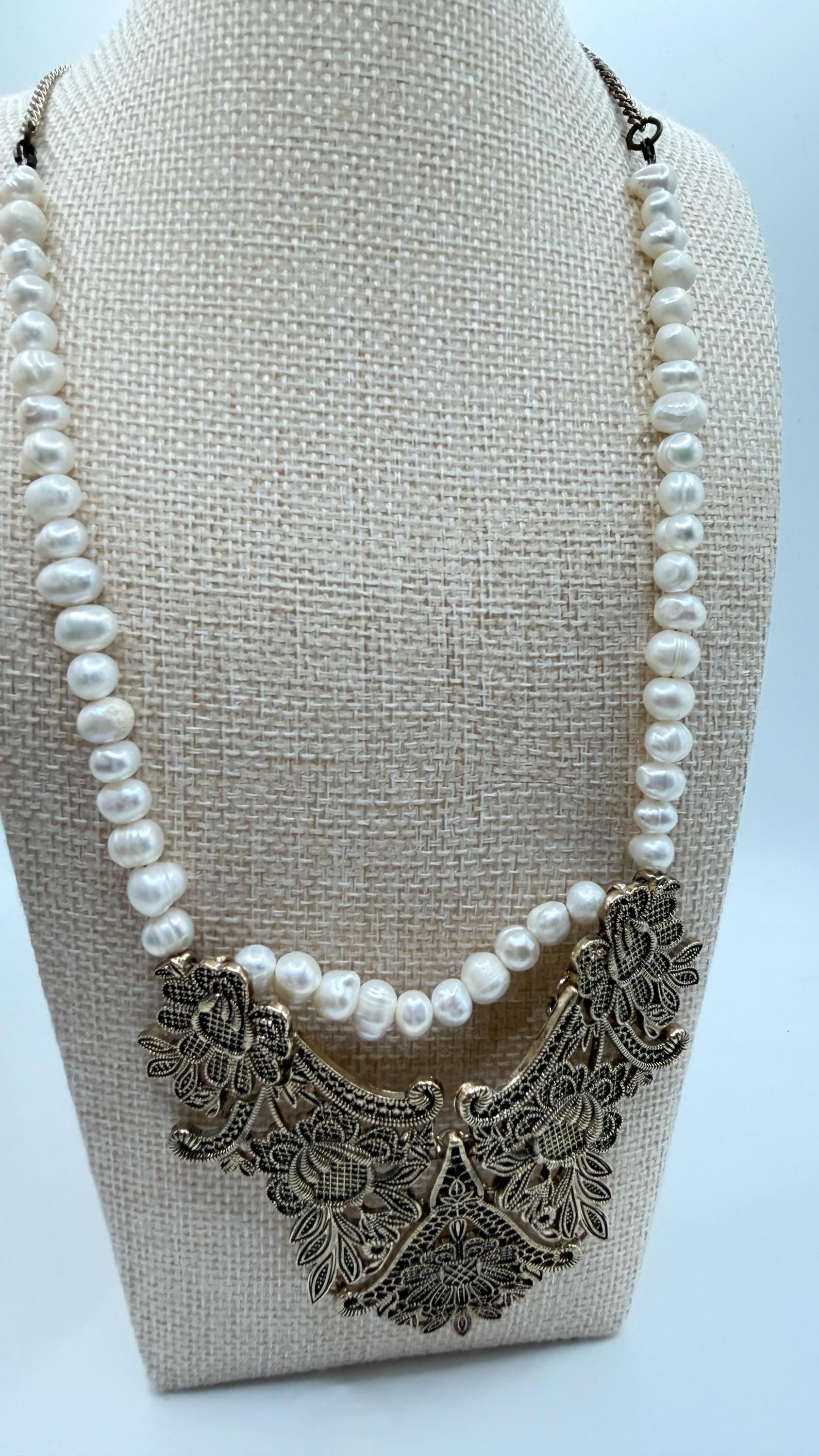 Pearl necklace with intricate metal clasp on a beige stand against a light blue background