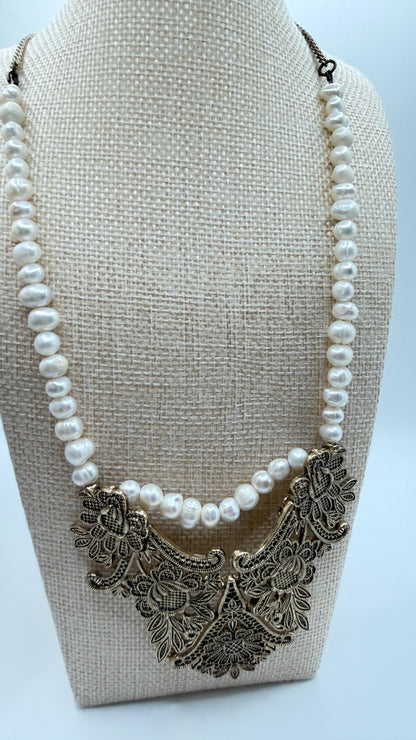 Pearl necklace with intricate metal clasp on a beige stand against a light blue background