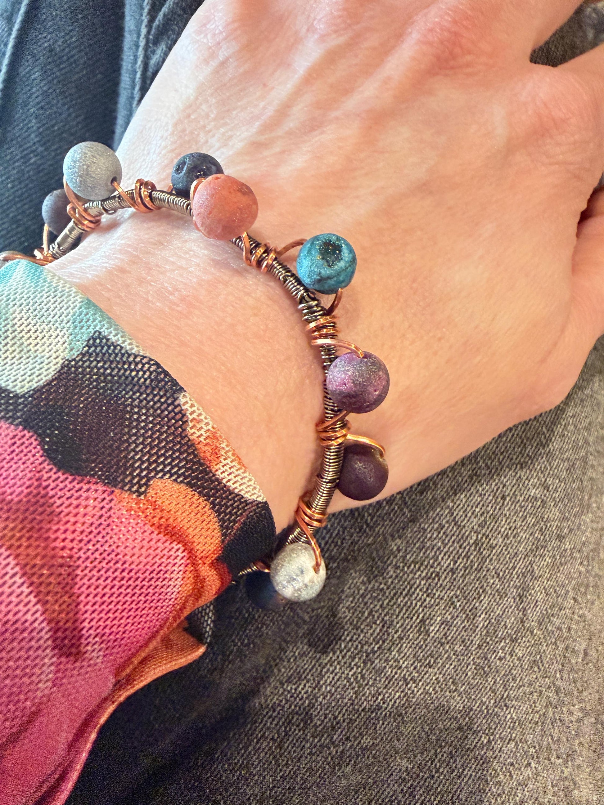 Close-up of a wrist wearing a colorful beaded bracelet with a multicolored fabric background.
