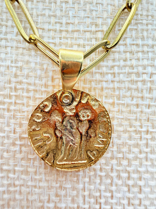 Gold necklace with a coin-shaped pendant on a textured beige background