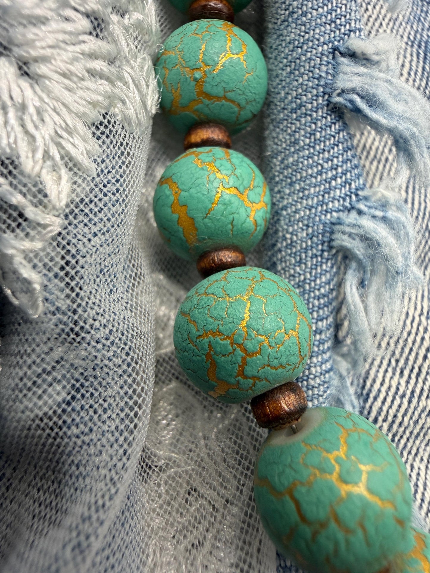 Turquoise beads with gold patterns on a fabric background