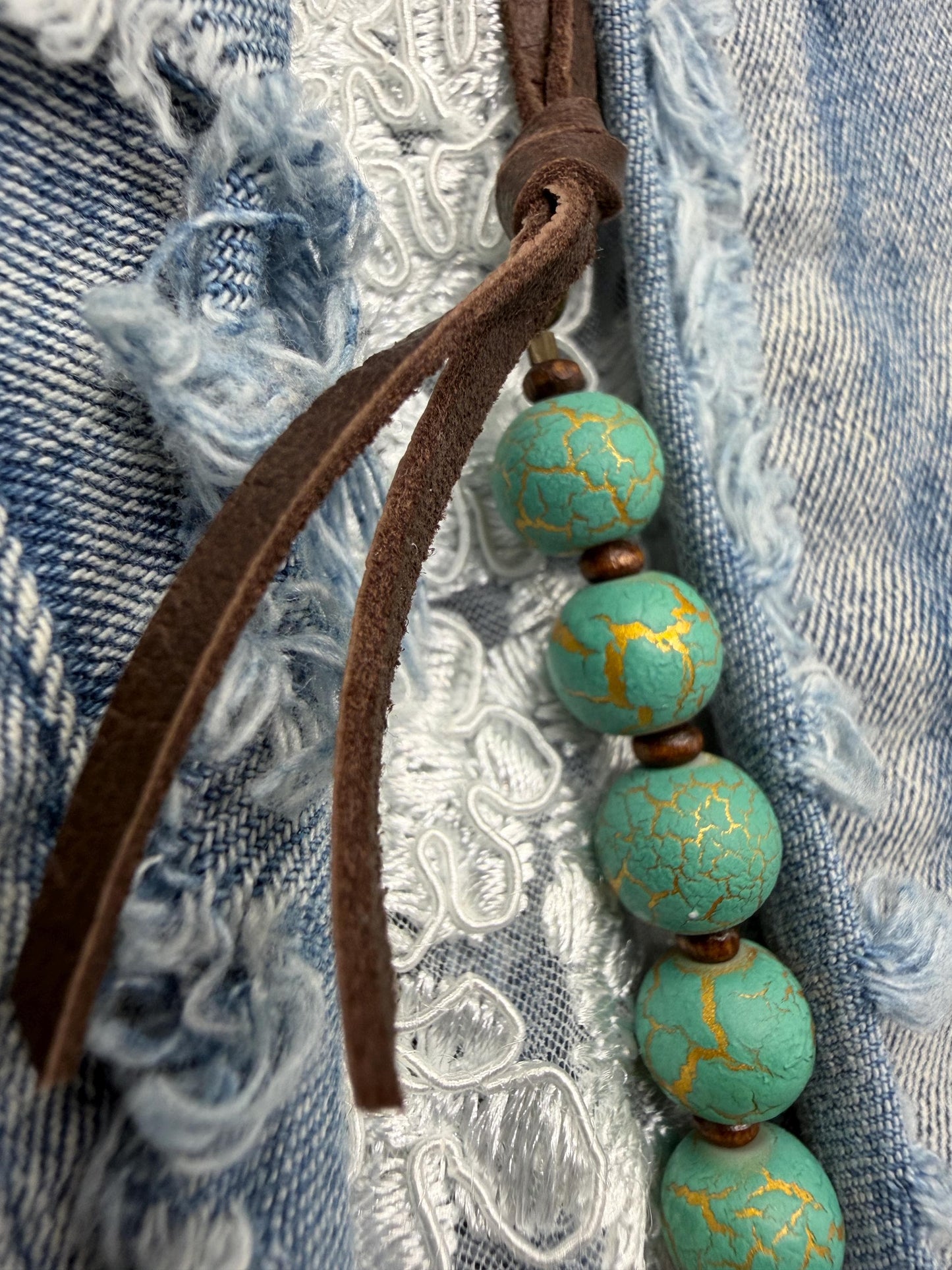 Turquoise beaded necklace with brown leather cord on a textured fabric background