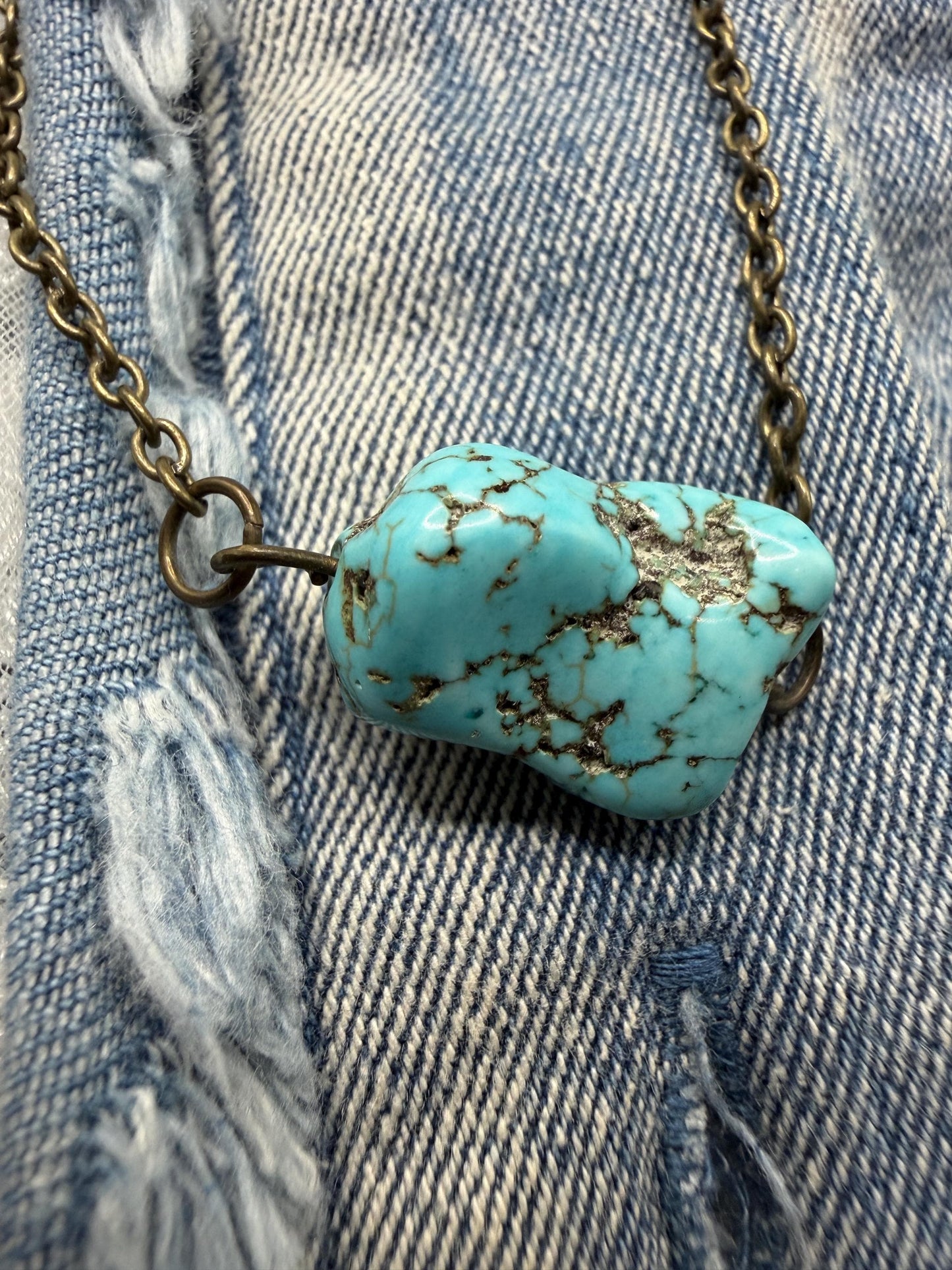Turquoise stone pendant on a chain against a denim background