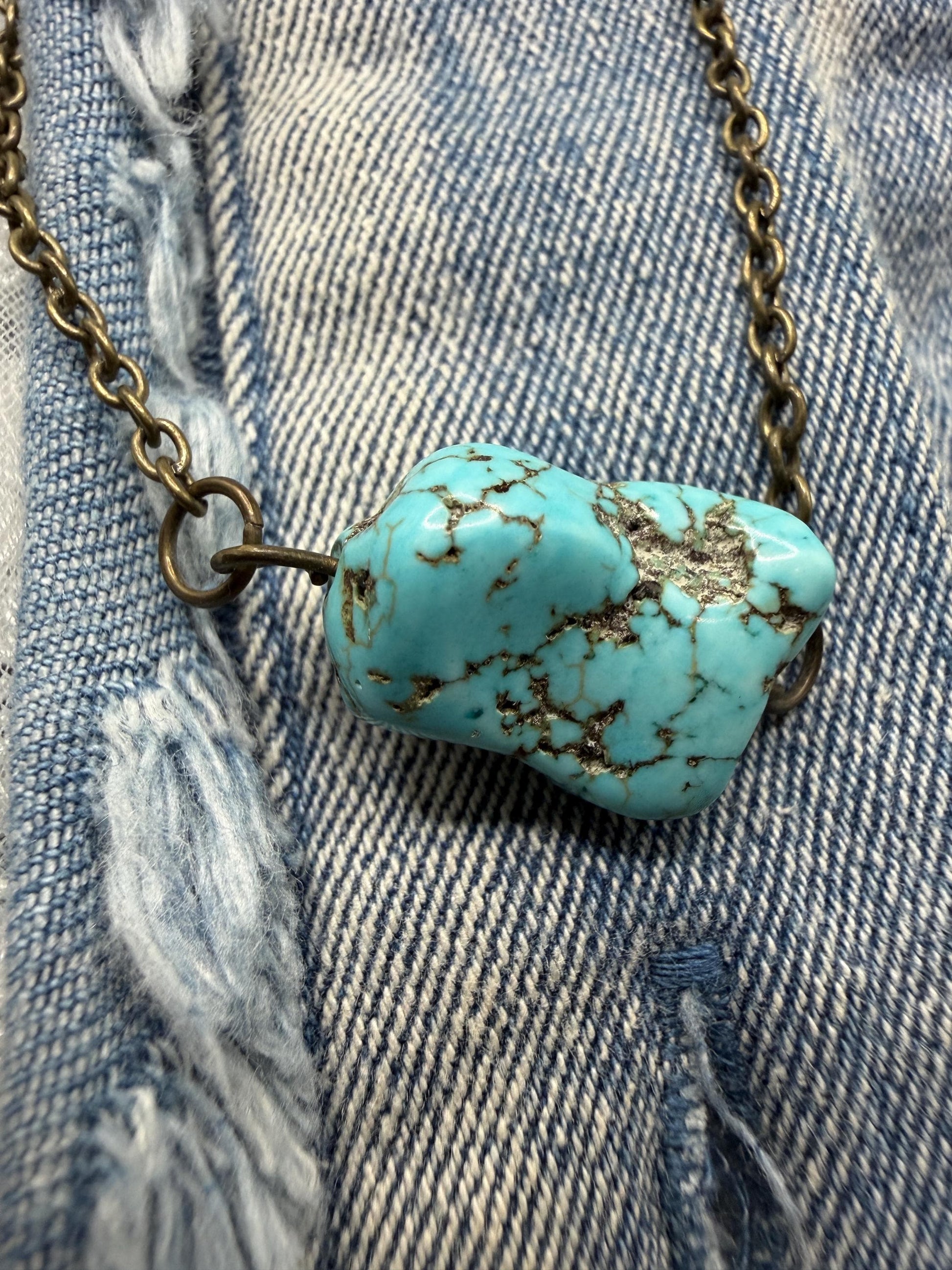 Turquoise stone pendant on a chain against a denim background