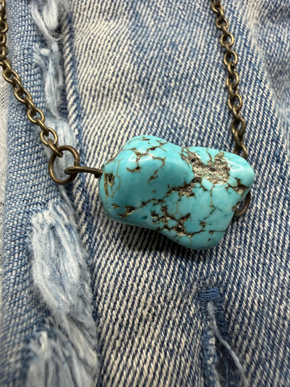 Turquoise stone pendant on a chain against a denim background