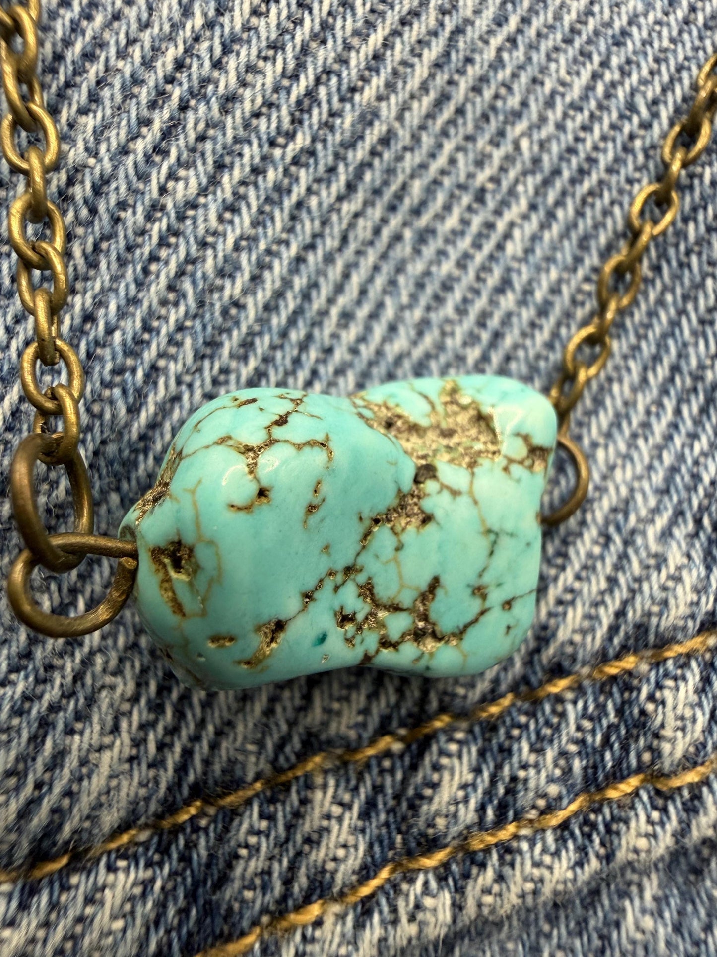 Turquoise stone necklace with gold chain on denim fabric