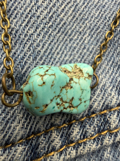 Turquoise stone necklace with gold chain on denim fabric