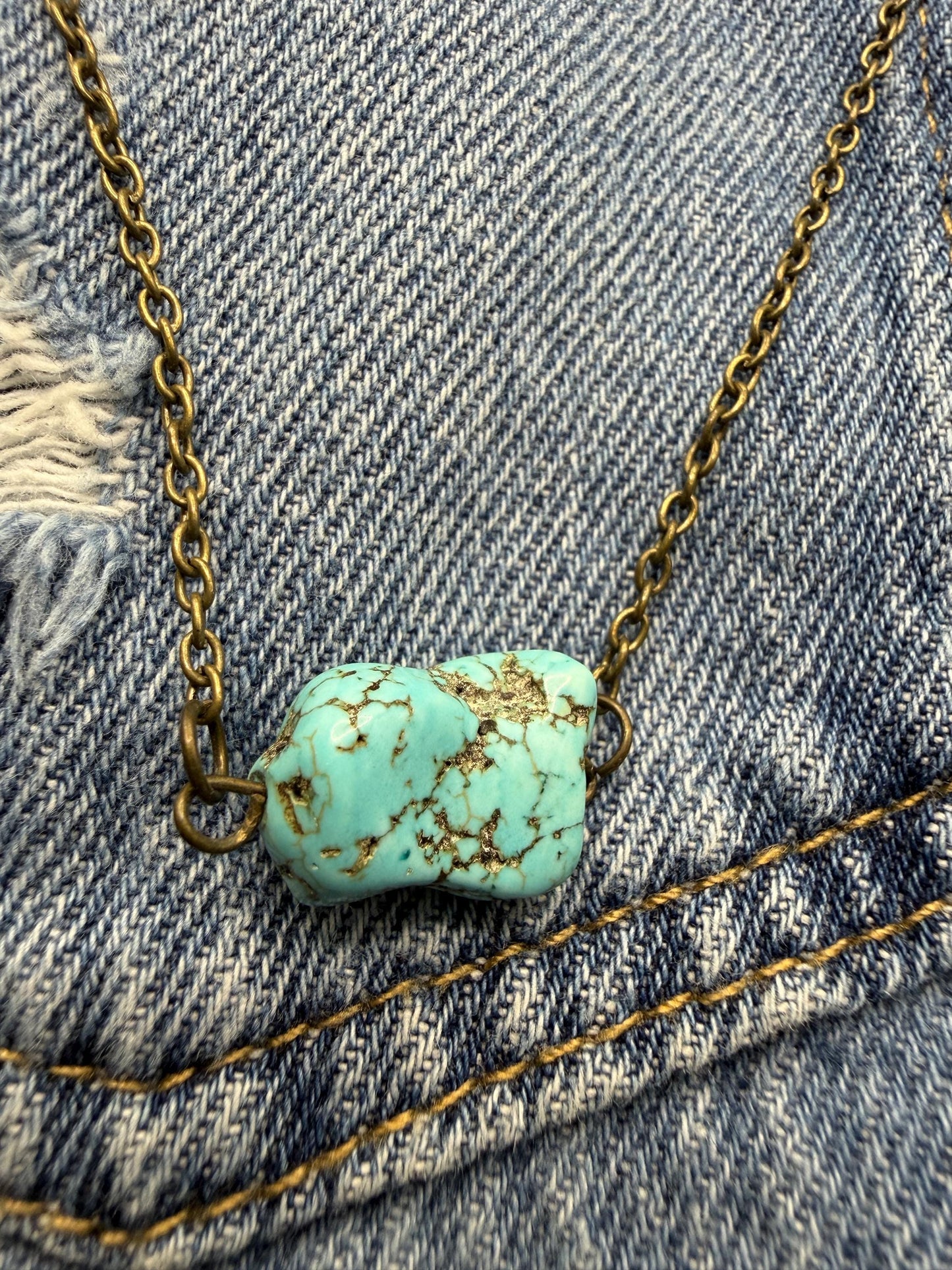 Turquoise stone necklace on a chain against a denim background