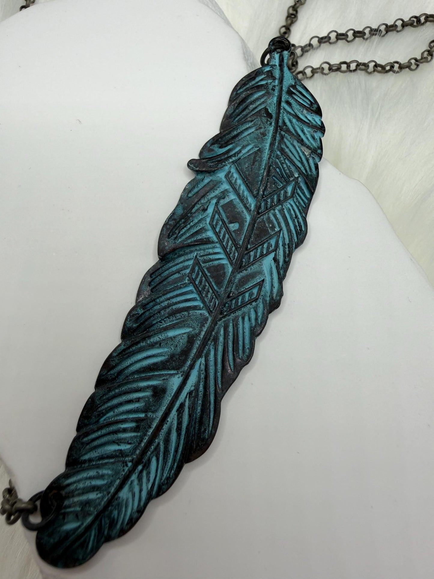Feather-shaped pendant with blue and black design on a white surface
