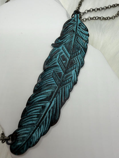 Feather-shaped pendant with blue and black design on a white surface