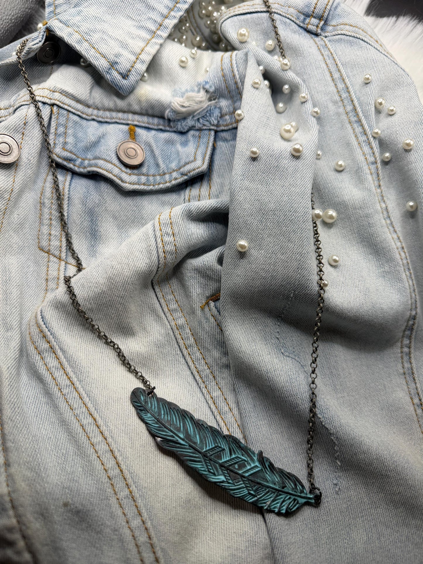 Blue denim jacket with pearl embellishments and a green feather necklace.