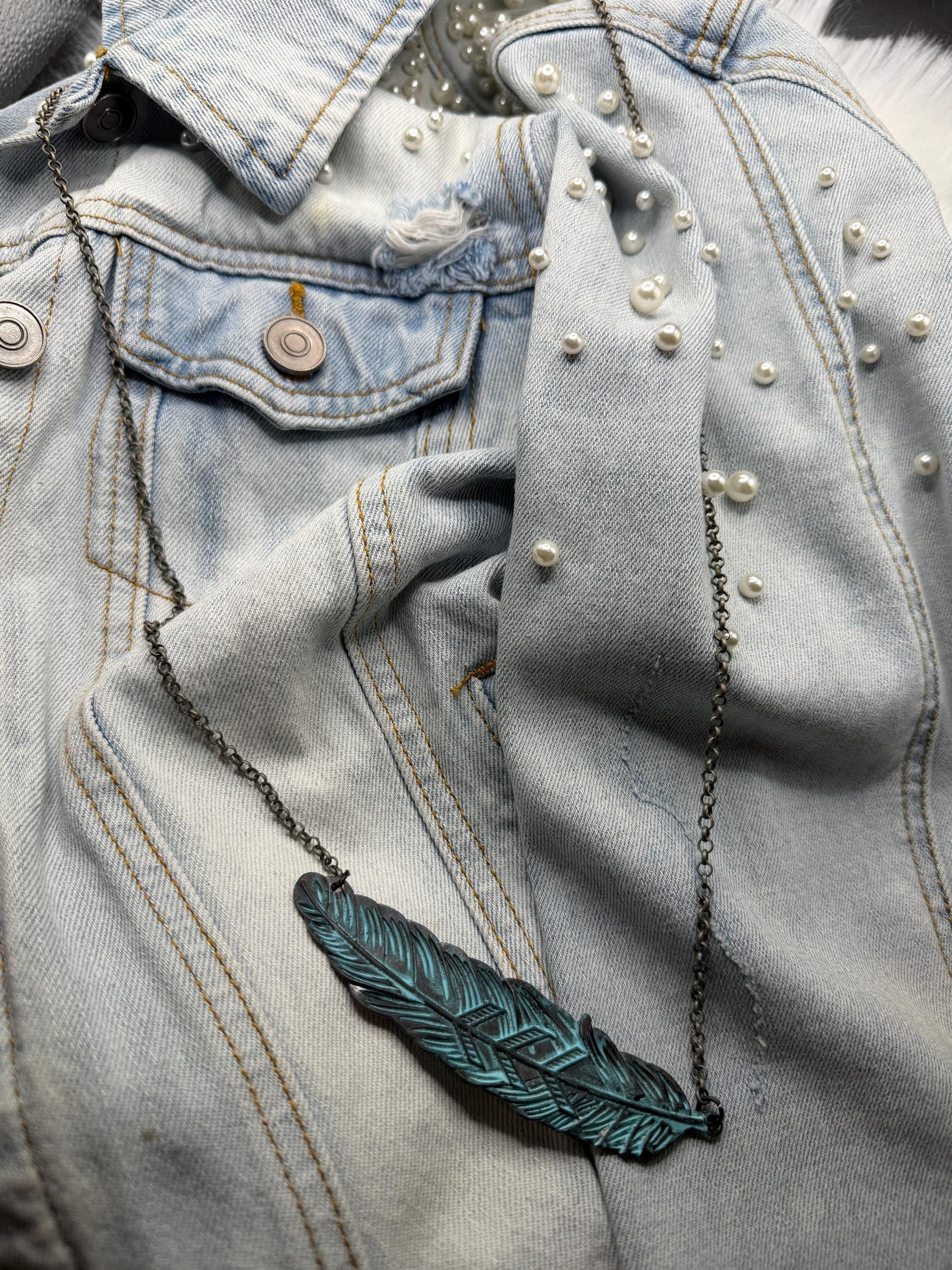 Blue denim jacket with pearl embellishments and a green feather necklace.
