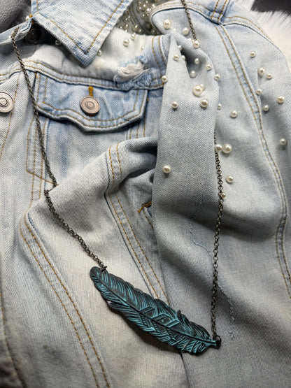 Blue denim jacket with pearl embellishments and a green feather necklace.