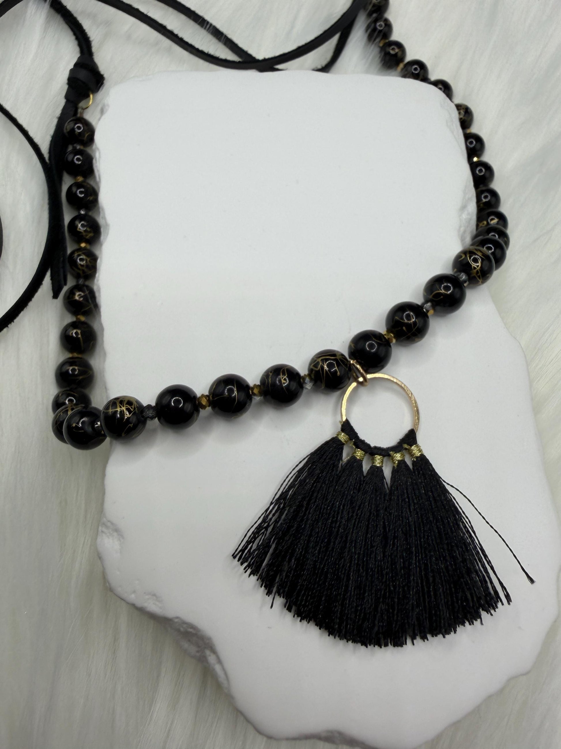 Black beaded necklace with a tassel pendant on a white stone surface