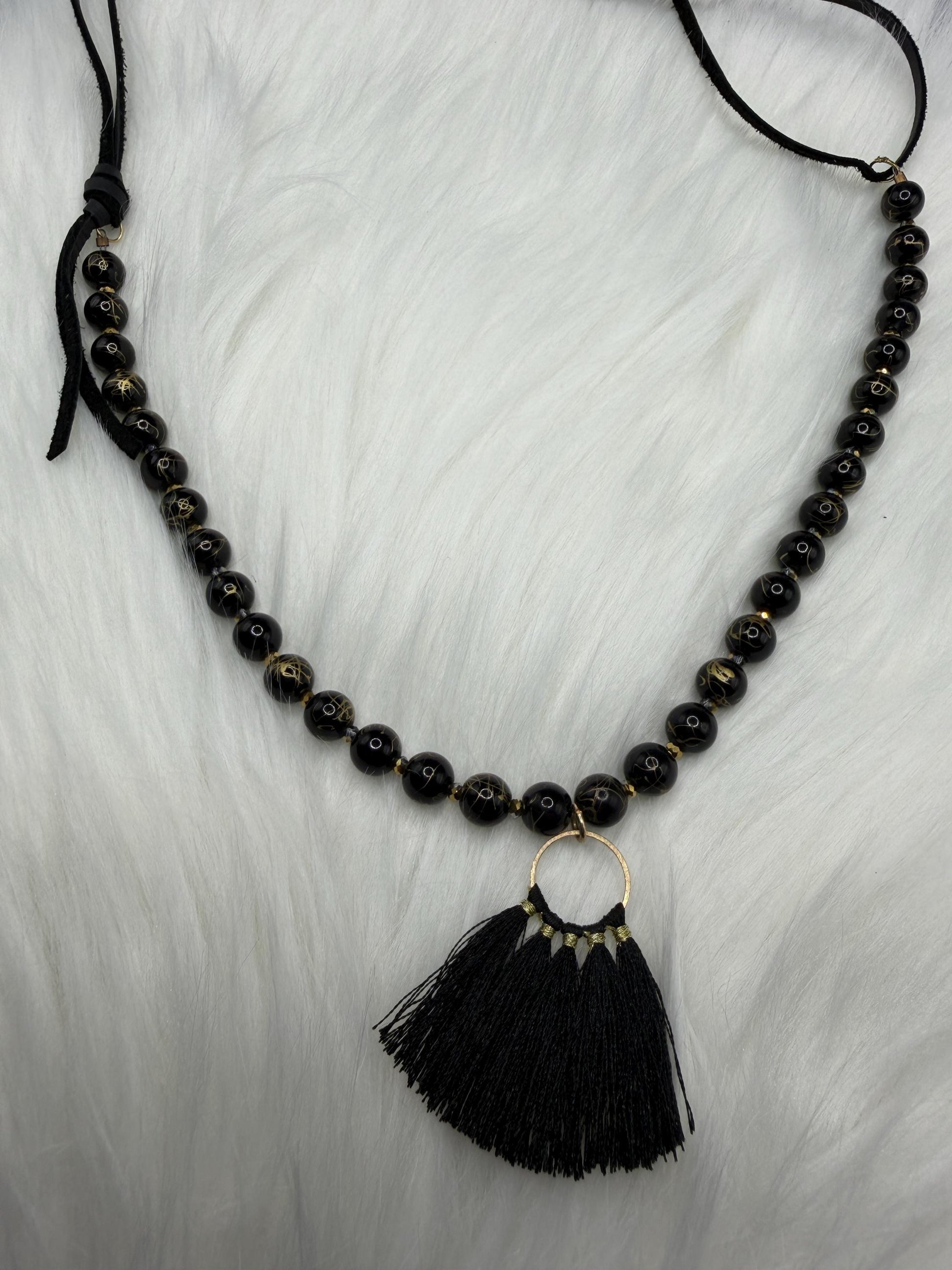 Black beaded necklace with a tassel pendant on a white background