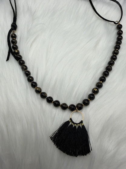Black beaded necklace with a tassel pendant on a white background