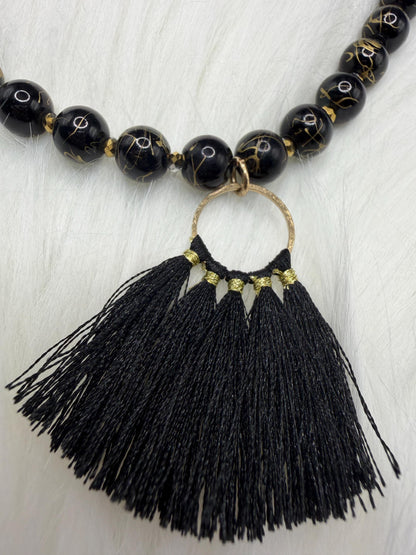 Necklace with black beads and tassel on a light wooden surface