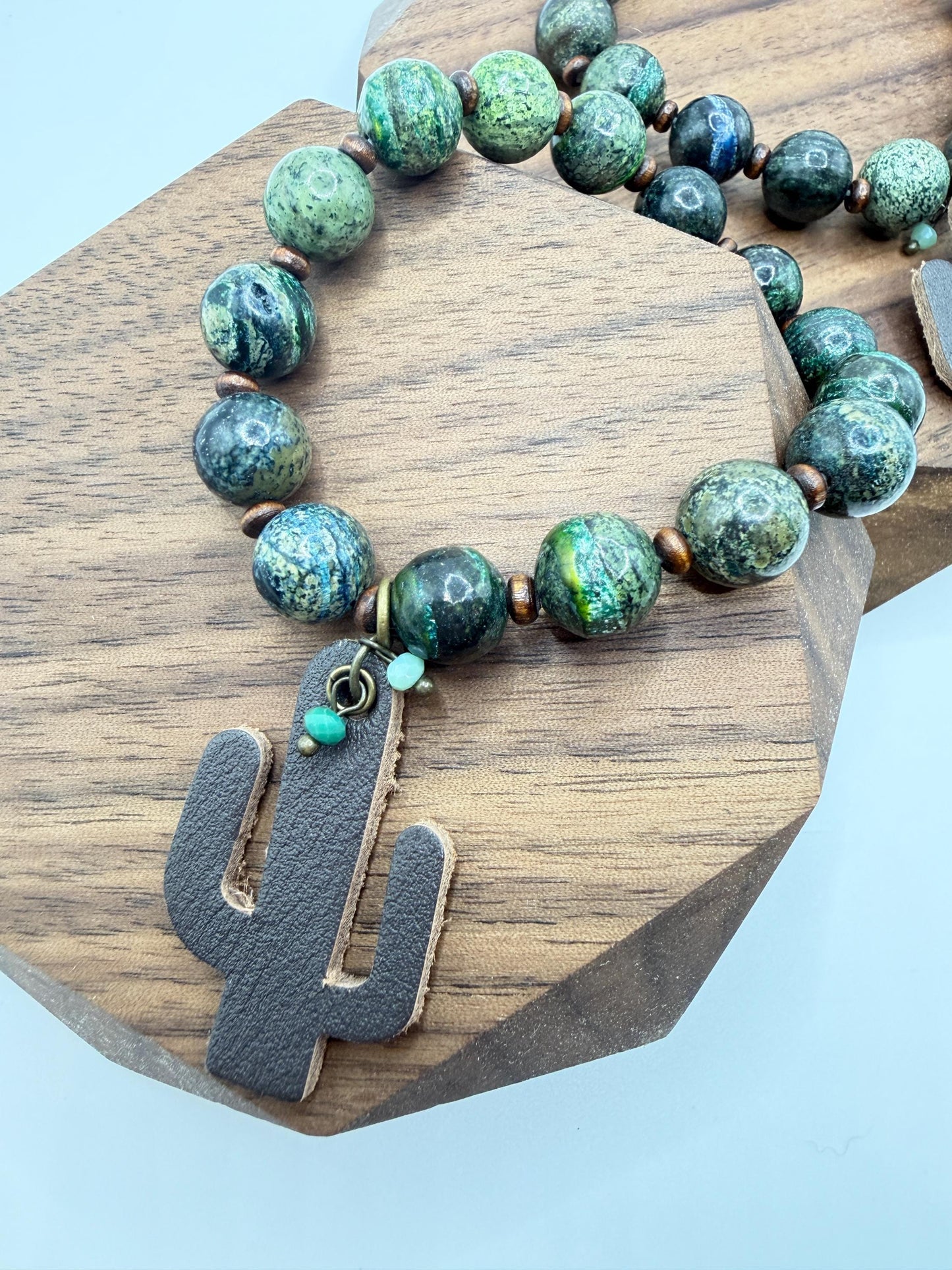 Green beaded bracelet with a cactus charm on a wooden surface