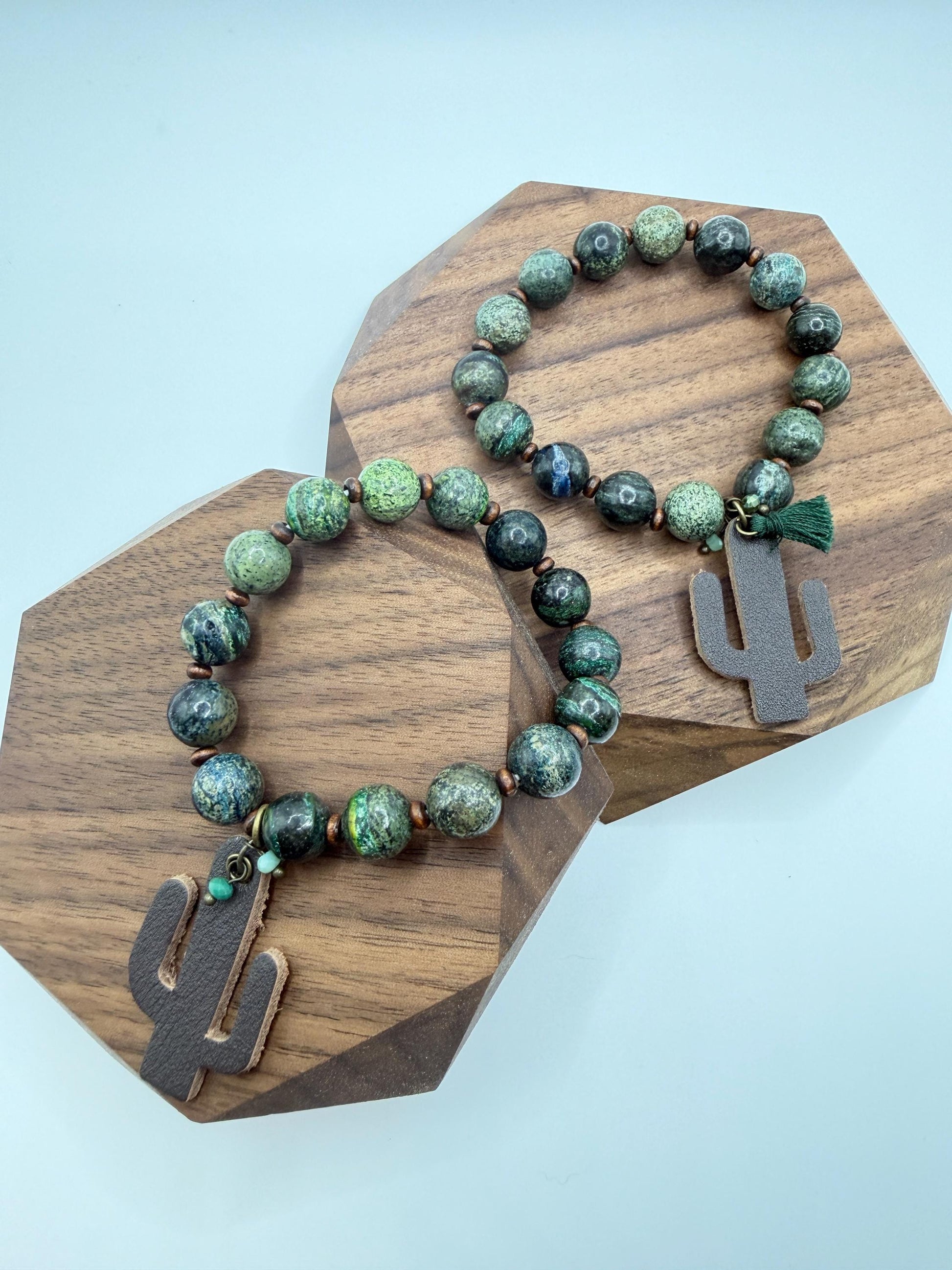 Beaded bracelet with cactus charm on a wooden stand against a light blue background