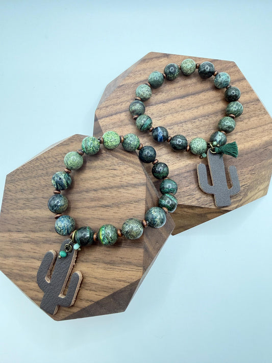 Beaded bracelet with cactus charm on a wooden stand against a light blue background