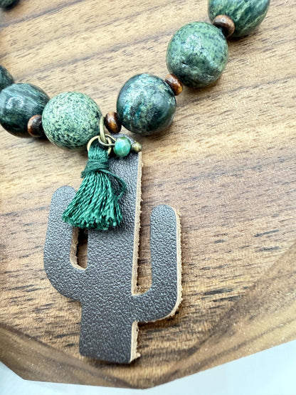 bracelet  with green beads and leather cactus charm on a wooden surface