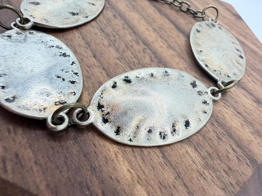 silver and bronze  bracelet with oval pendants on a wooden surface