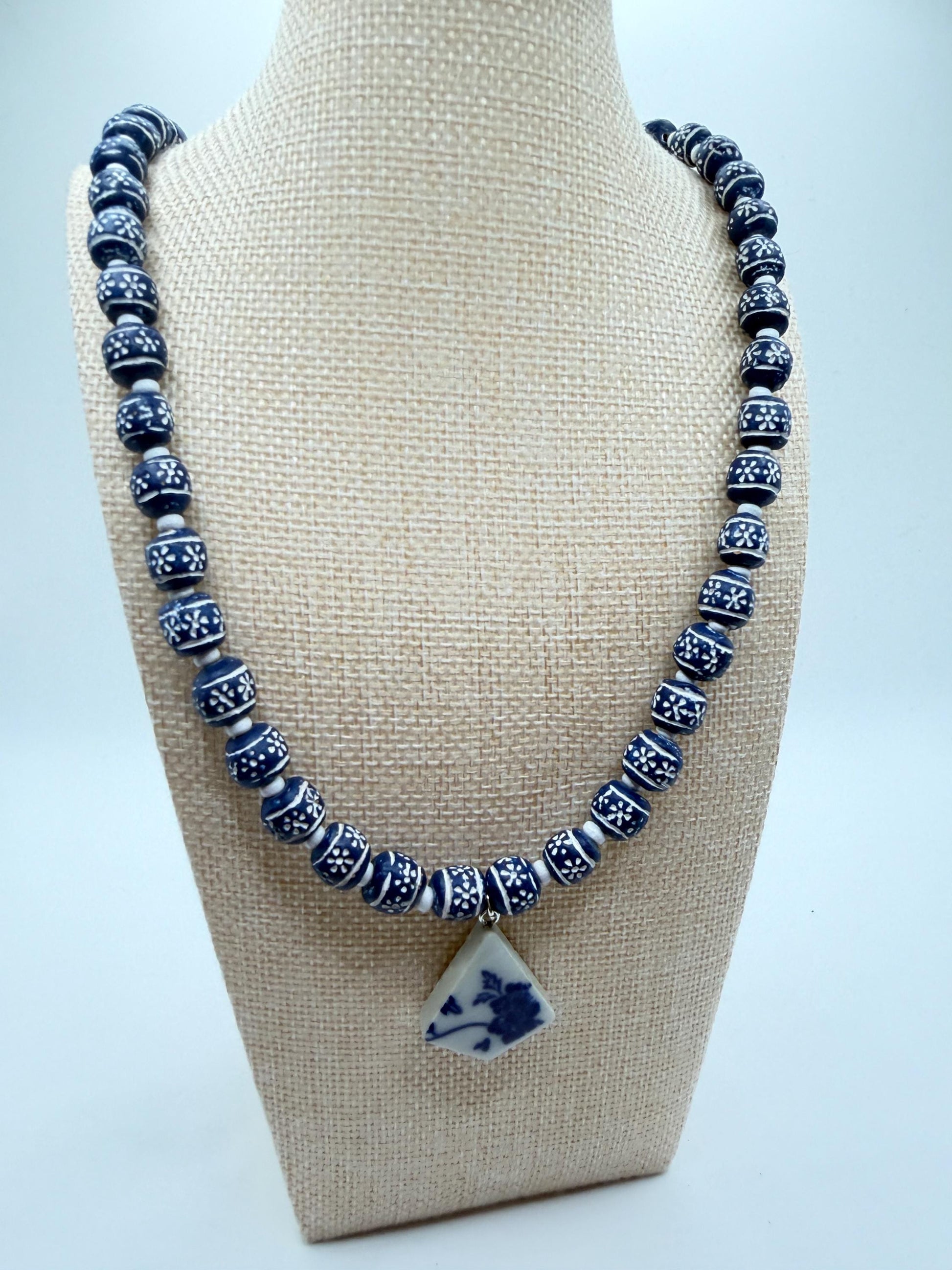 Necklace with blue and white beads on a beige stand against a light gray background