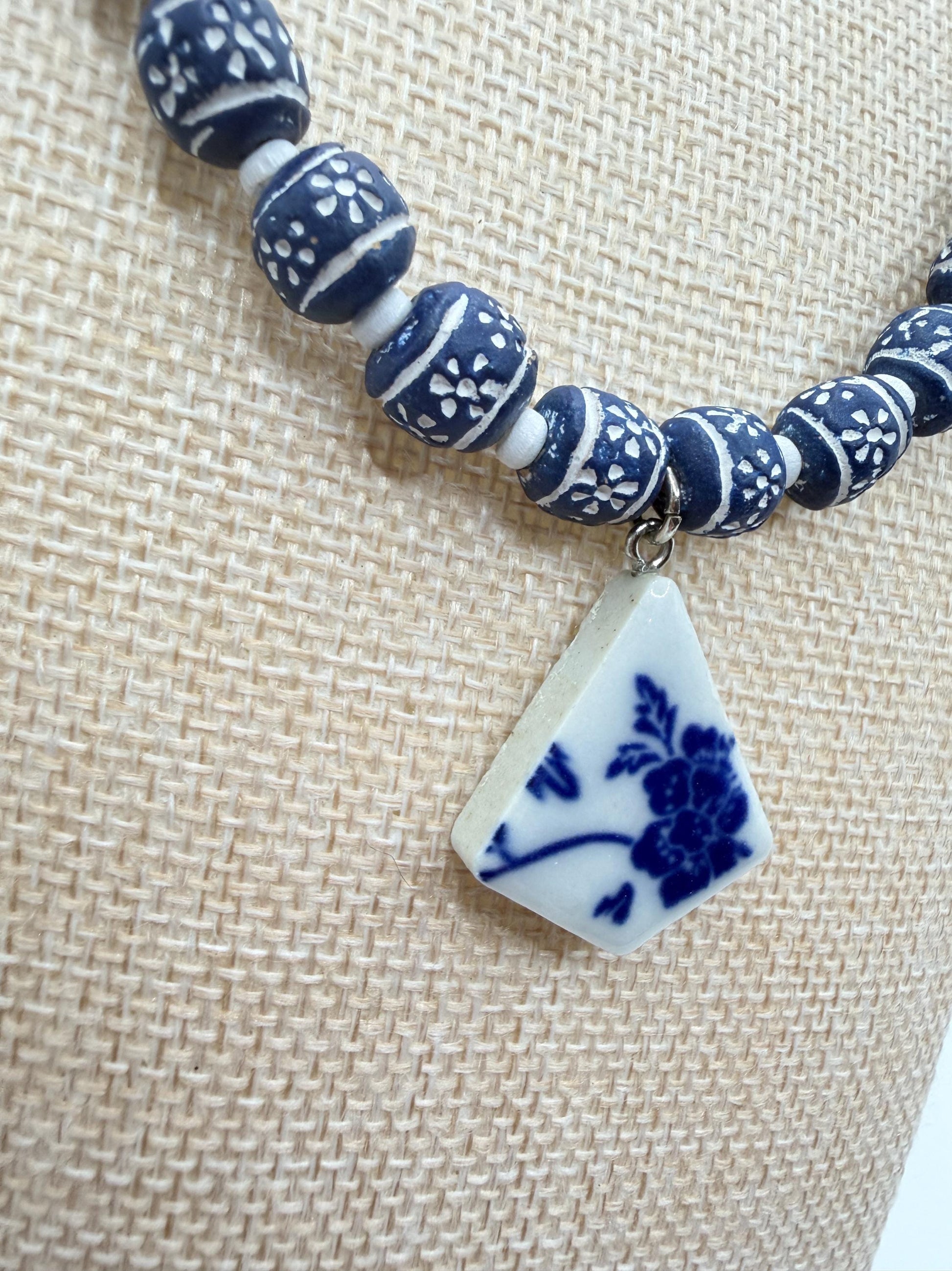 Bracelet with blue and white beads and a floral pendant on a textured beige background