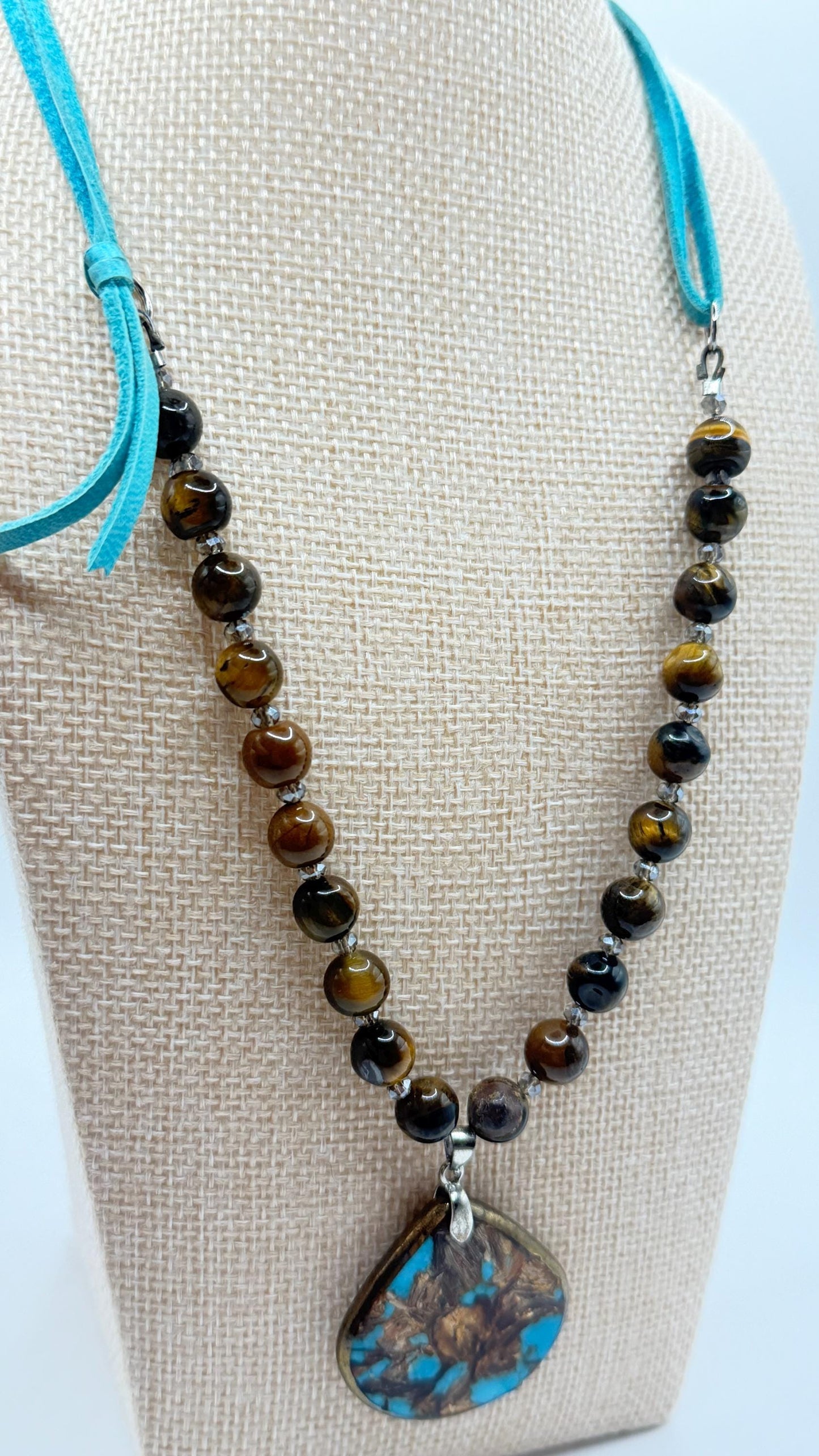 Necklace with beads and a turquoise pendant on a mannequin bust.