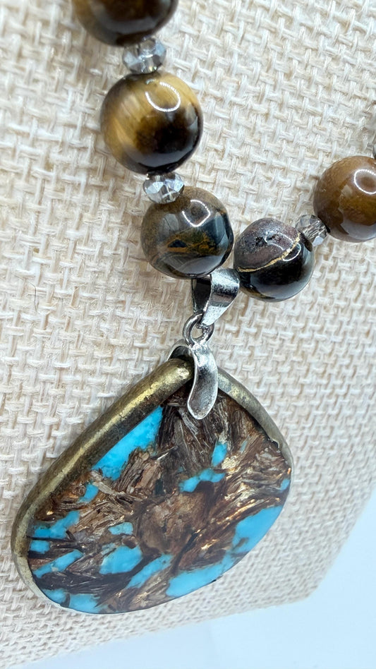 Necklace with brown beads and a turquoise pendant on a textured fabric background