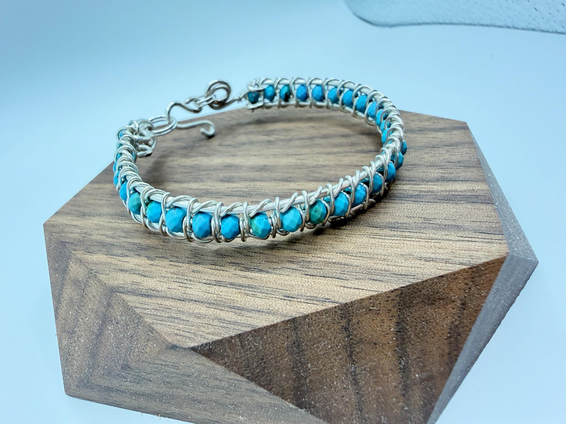 wire wrapped Turquoise beaded bracelet on a wooden block with a light blue background