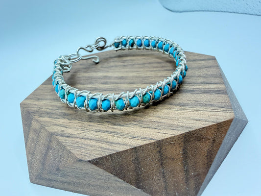 wire wrapped Turquoise beaded bracelet on a wooden block with a light blue background