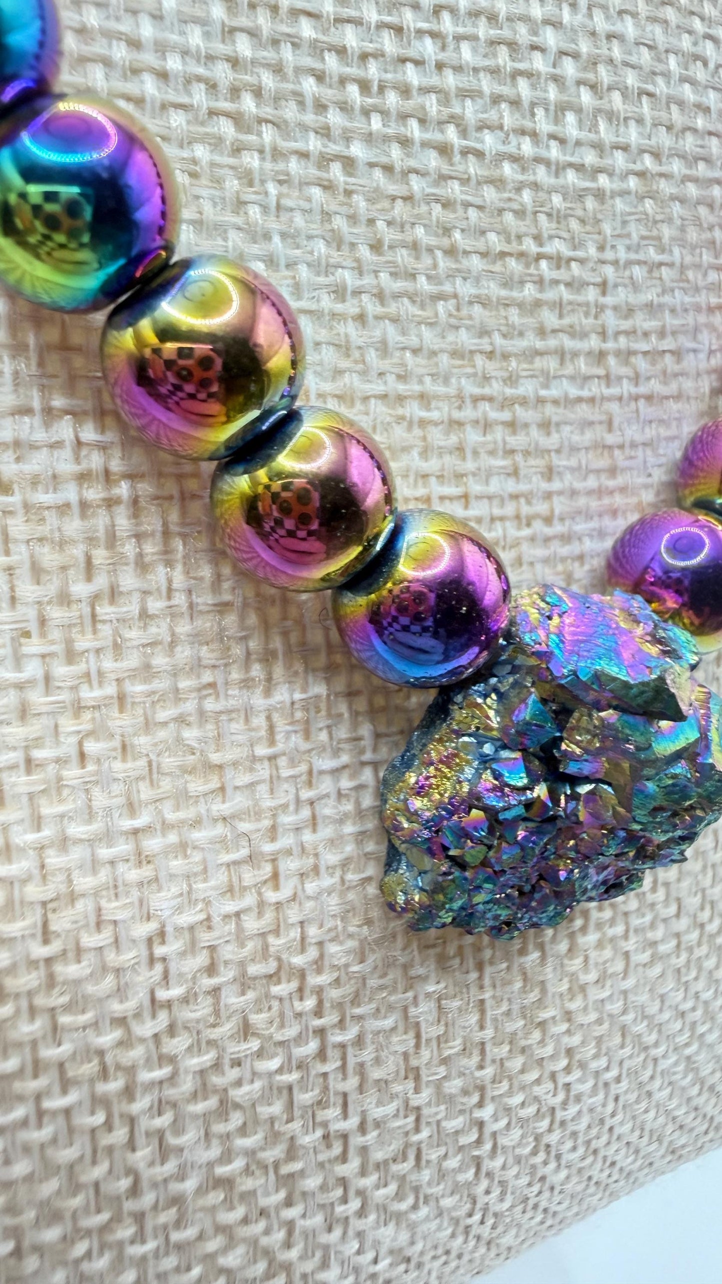 Multicolored beaded bracelet with a large iridescent bead on a textured beige background