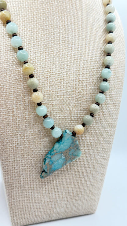 Beaded necklace with a large turquoise stone pendant on a beige display stand.