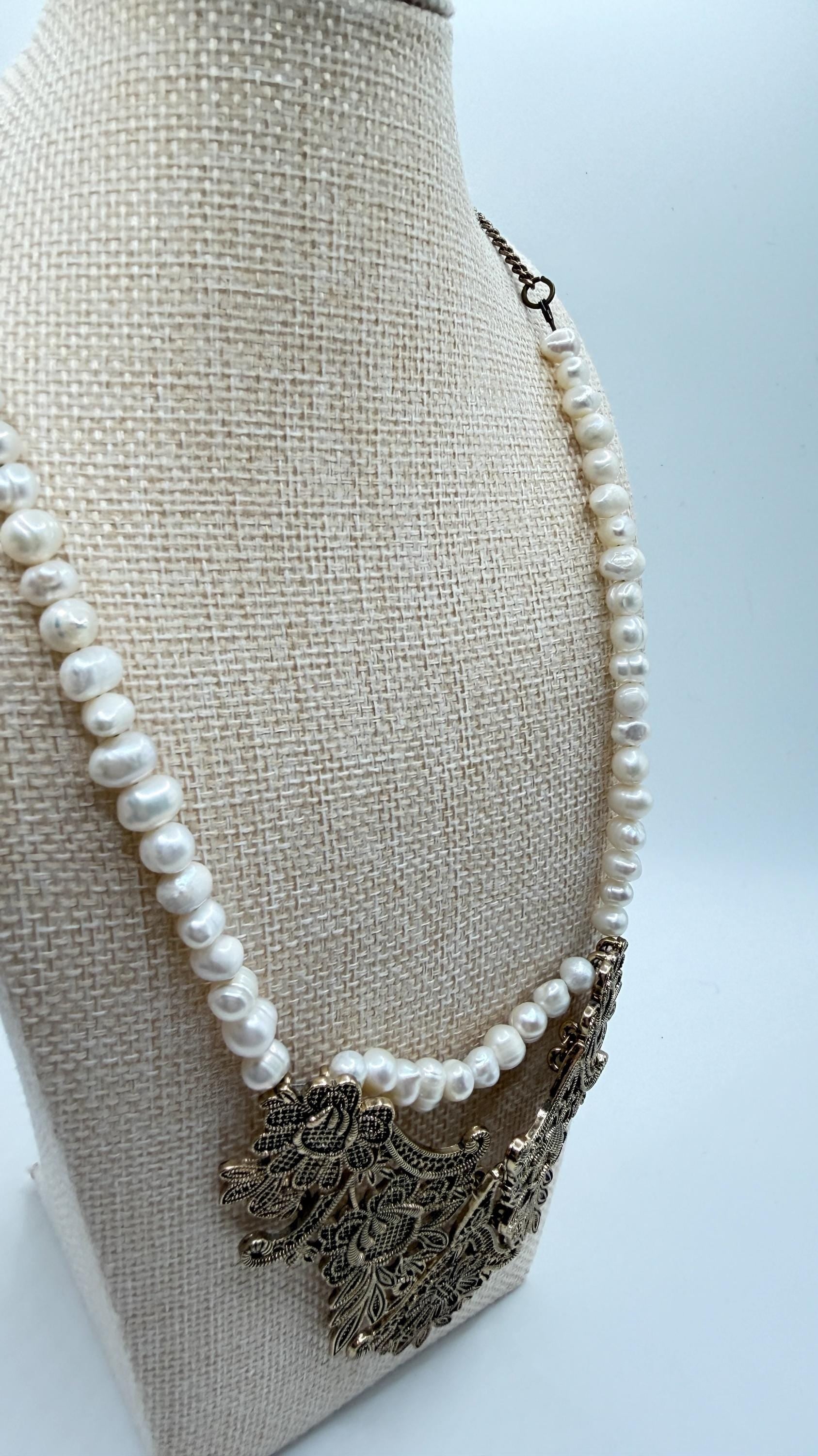 Pearl necklace with an ornate metal pendant on a beige mannequin bust.
