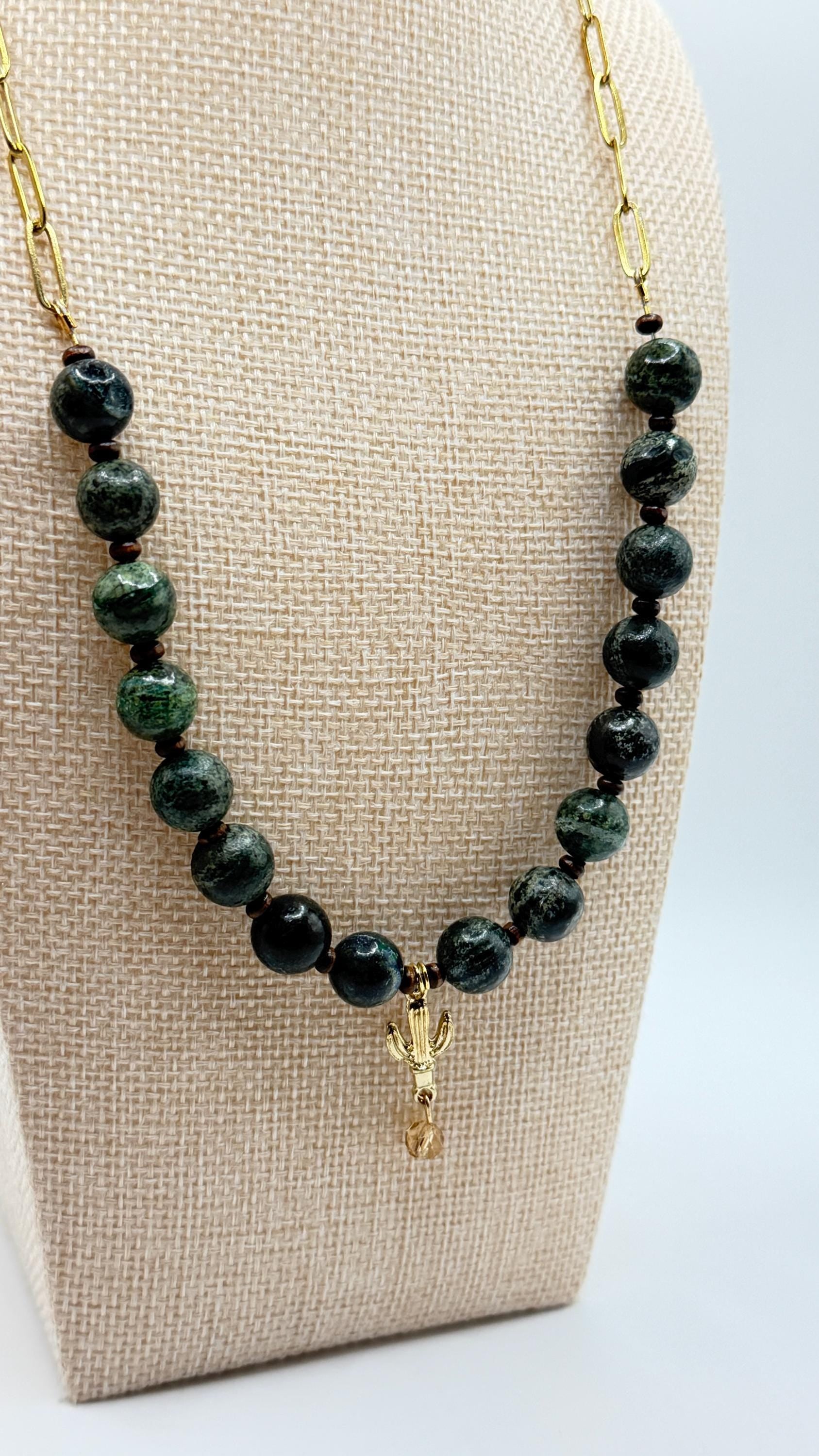 Necklace with green beads and a gold charm on a beige display stand.