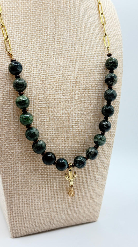 Necklace with green beads and a gold charm on a beige display stand.