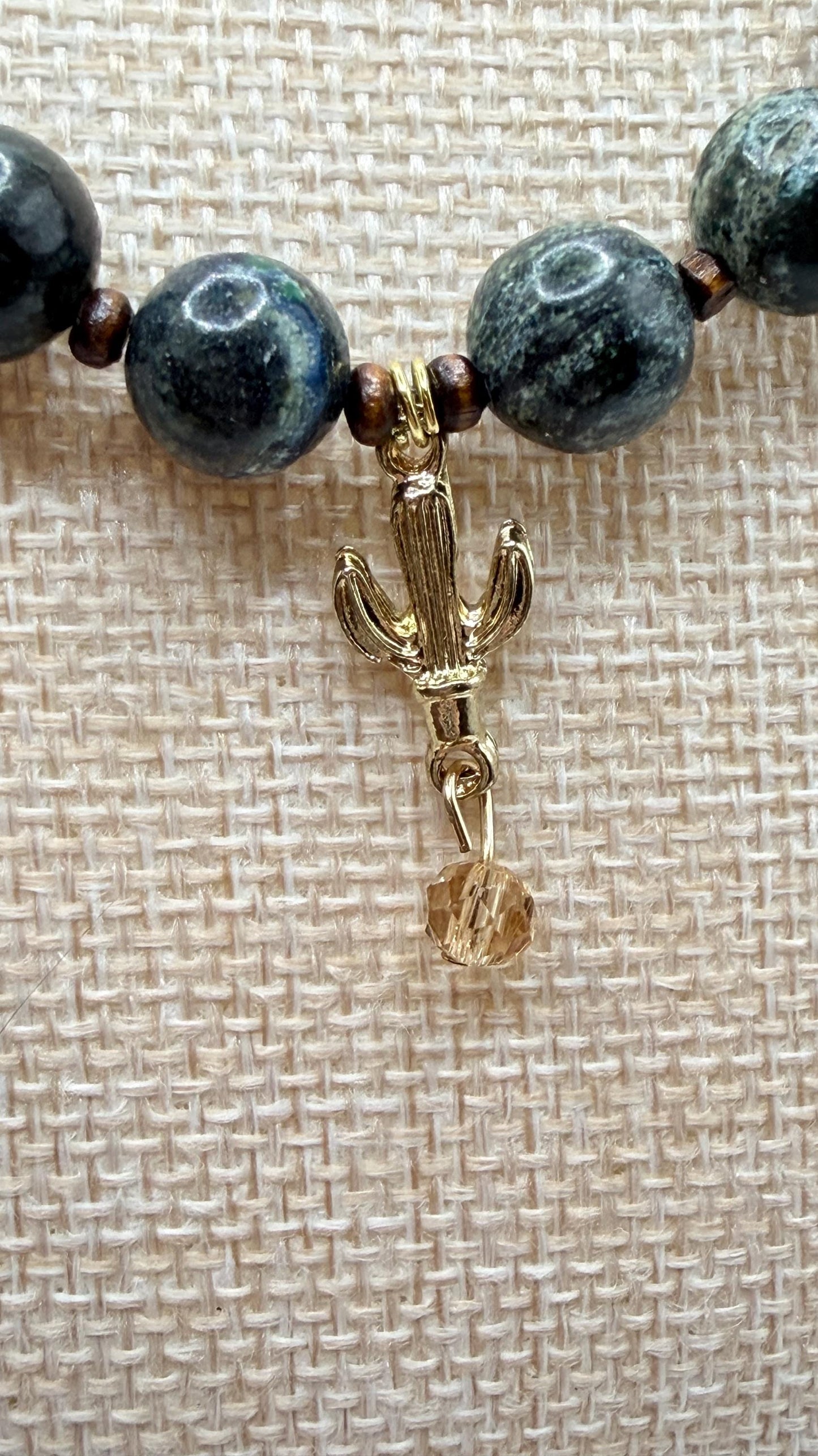 Necklace with blue beads and a gold cactus charm on a textured beige background
