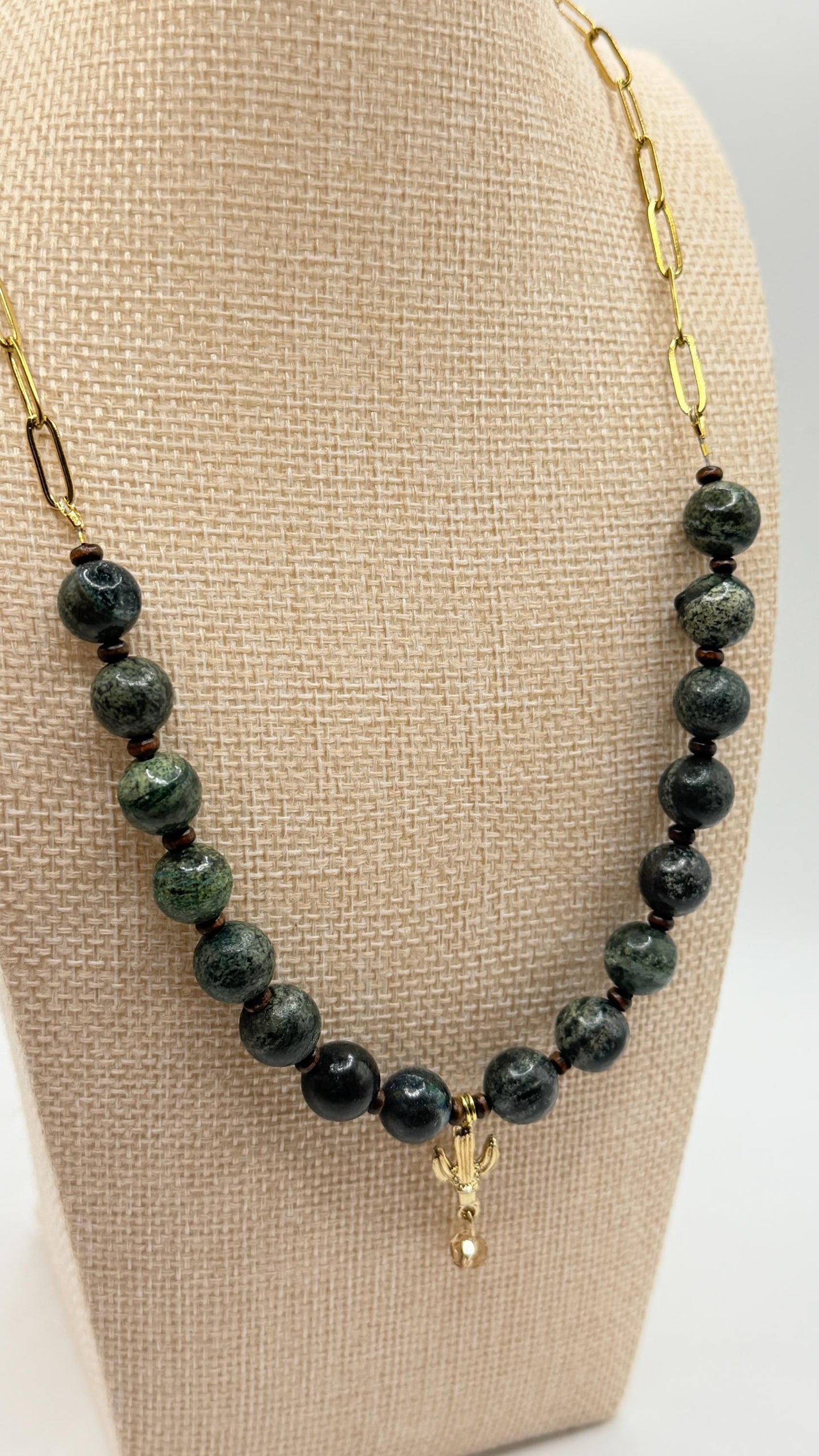Necklace with green beads and gold chain on a beige display stand