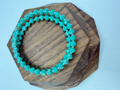 Turquoise beaded bracelet on a wooden hexagonal block against a light blue background